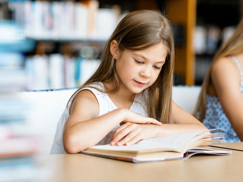 little girl reading at table